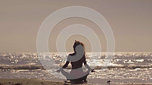 The girl practic yoga on the beach at sunset. Young girl doing exercise at a tropical beach. Silhouette of a woman yoga