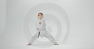 The girl practices karate at home. The child is dressed in a kimono on a white background.