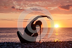 Girl practicing yoga on the beach. View from the back, sunset