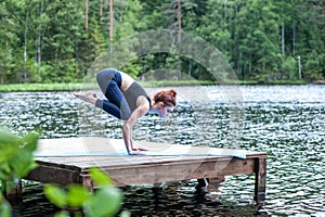 Girl practicing yoga, doing Bakasana exercise, Crane pose,  on the lake.   Concept of healthy life and natural balance