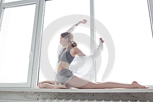 Girl practicing yoga, doing splits, stretching exercise on windowsill at home