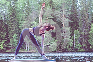 Girl practicing yoga, doing Utthita Trikonasana exercise, extended triangle pose  on the lake. The concept of appeasement,