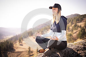 Girl is practicing yoga at mountain. Happy woman on the sunset in nature in summer sitting on the ground.