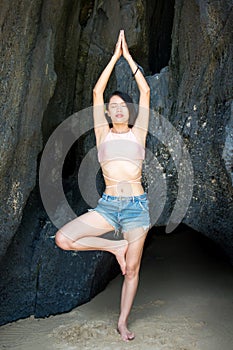 Girl practicing yoga in the shade of a beach cave