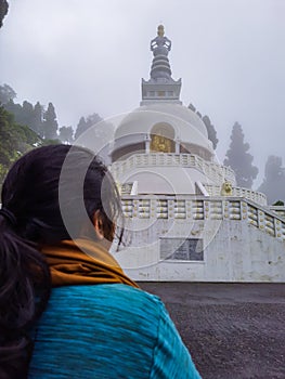 Girl praying at buddhist shanti stupa covered with misty fog at morning from different angle