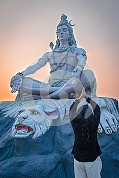 Girl praying at hindu god lord shiva statue in meditation posture with dramatic sky at evening