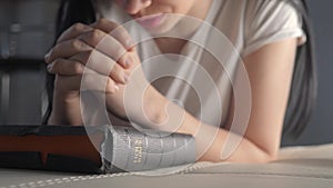 Girl praying indoors at bedtime on lifestyle bible. religion concept evening prayer woman brunette hands on bible