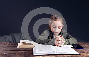 The girl prays with folded hands. An open Holy Bible on the table. Pray the prayer