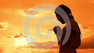 The girl prays. Girl folded her hands in prayer silhouette at sunset. slow motion video. Girl folded her hands in prayer