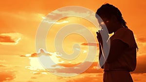 The girl prays. Girl folded her hands in prayer silhouette at sunset. slow motion video. Girl folded her hands in prayer