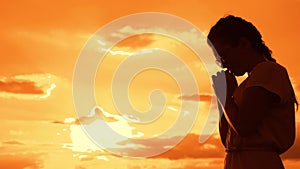 The girl prays. Girl folded her hands in prayer silhouette at sunset. slow motion video. Girl folded her hands in prayer