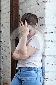 Girl of pre-teen age  sad near white wall covering her face