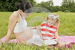 Girl with pregnant mother reading a book