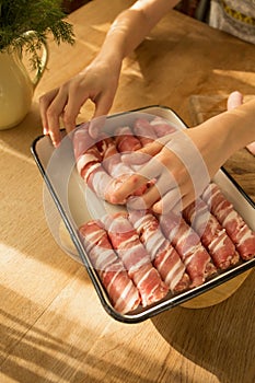 A girl prepares a traditional Christmas dish Pigs in a blanket Wraps sausages in bacon