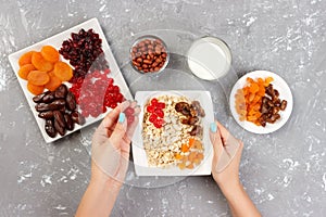 The girl is preparing her muesli for breakfast. The girl puts herself a dried fruit in oatmeal porridge. Useful and healthy breakf