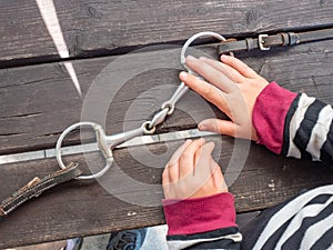 Girl preparing steel horse snaffle-bit on wooden table