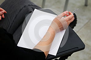 A girl is preparing to fill out a blank form, write an essay or dictation, sitting on a school chair with a writing stand. View