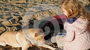 Girl preschool girl on the beach feeds the dog. Spring