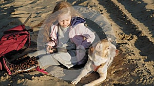 Girl preschool girl on the beach feeds the dog. Spring