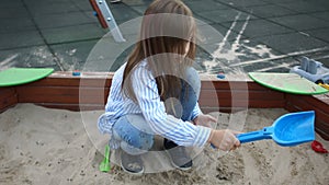 Girl preschool girl with long hair plays in the sandbox with a shovel and apiary. Happy childhood. Weekdays at the
