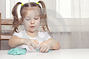 Girl preschooler sits at a table and sculpts from turquoise dough for sculpting