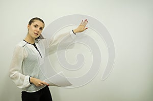 girl is presenting something while standing on the left against a white wall holding sheets in one hand