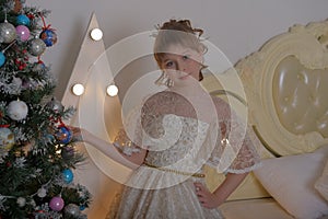 Girl princess in alabaster victorian dress by christmas tree in christmas