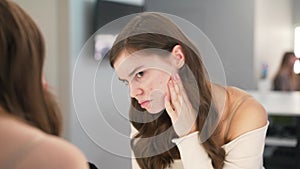 Girl with the problem of acne during puberty, looks at herself in the mirror. Close-up