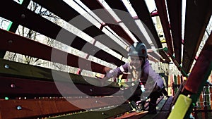 Girl in protective climbing gear overcomes a tunnel made of wooden planks in a cable car Park