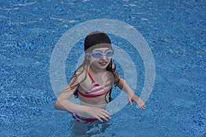 Girl with protective goggles and red swimsuit splashing in swimming pool. Adorable little girl in outdoor swimming pool