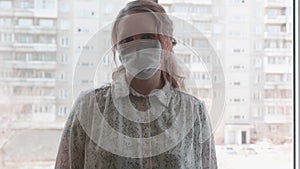 A girl in a protective mask stands near a window in the hospital. Prevention and protection of health and safety of life