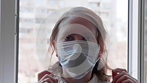 A girl in a protective mask stands near a window in the hospital. Prevention and protection of health and safety of life