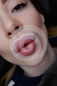 A girl pulls her lips forward before a permanent lip makeup procedure