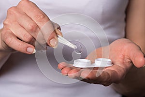 Girl pulls a soft contact lens out of the container with tweezers