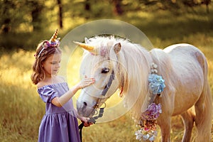 Girl in purple dress with wreath of a unicorn in hair hugging and kissing white unicorn. Dreams come true. Fairy tale