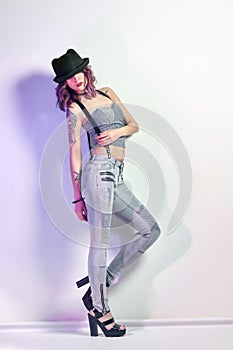 girl with purple hair and a tattoo on the body posing on grey background. Perfect woman in gray jeans and a t-shirt, bright