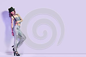 girl with purple hair and a tattoo on the body posing on purple background, lettering place. Perfect woman in gray jeans