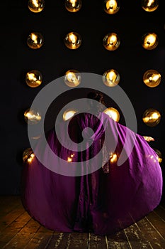Girl in purple mantle poses near wall with lamps photo