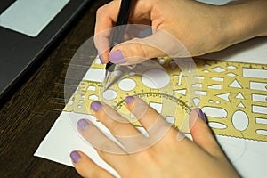 Girl with purple nails draws a circle with a ruler with figures