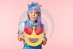 Girl in purple wig holding infatuation emoticon isolated on pink