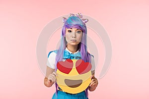 Girl in purple wig holding infatuation emoticon isolated on pink