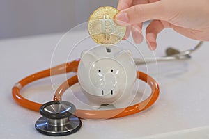 The girl put a bitcoin into the white piggy bank on orange stethoscope , saving for healthcare