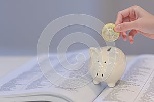 The girl put a bitcoin into the white piggy bank on text book, saving for education