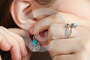 The girl puts on a earring with a turquoise stone on her ear