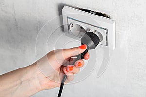 The girl puts the electric plug into a broken socket. Risk of electric shock, close-up