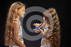 A girl puts jar cream on her finger, another girl sits nearby