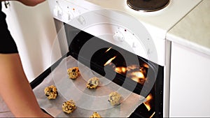 Girl puts in the oven a baking sheet with American cookies with chocolate chips