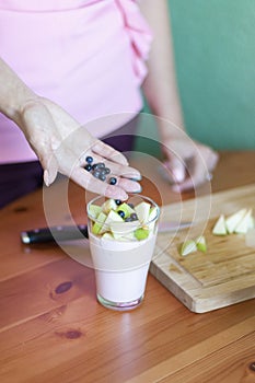 The girl puts the pieces of green apples in a glass of yogurt