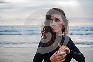 The girl puts zinc before surfing. Close up shot of beautiful girl with pink zurf zinc mask, dressed in black wetsuit, enjoys