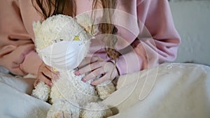 A girl is putting on a face mask on a Teddy Bear for protect from coronavirus. Pandemia of covid-19. Save From Toxic gas, virus or